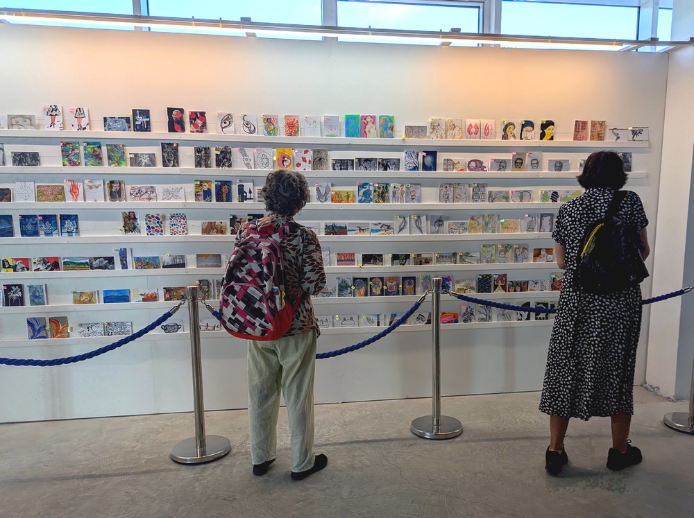 מבקרות מתבוננות בגלויות בתערוכת הגלויה הסודית, יריד צבע טרי, 2024